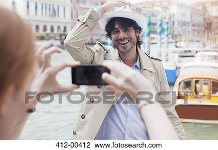 Stock Image - Woman with camera phone photographing man at waterfront in Venice. Fotosearch
