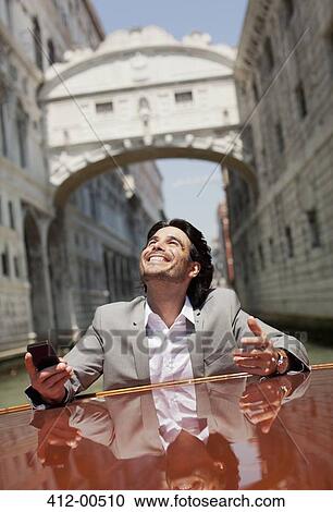 Stock Image - Enthusiastic businessman riding on boat through canal in Venice. Fotosearch