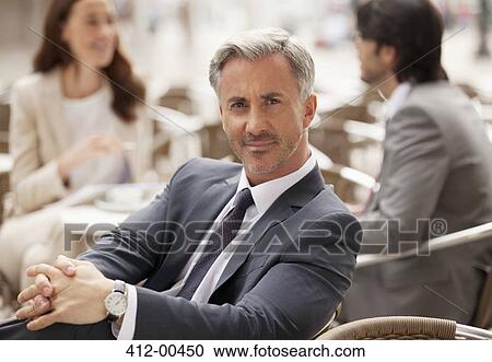 Portrait of smiling businessman at sidewalk cafe with co-workers in background View Large Photo Image Stock Image - Portrait of smiling businessman at sidewalk cafe with co-workers in background. Fotosearch