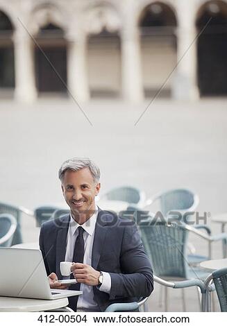 Portrait of smiling businessman drinking espresso and using laptop at sidewalk cafe View Large Photo Image Picture - Portrait of smiling businessman drinking espresso and using laptop at sidewalk cafe. Fotosearch