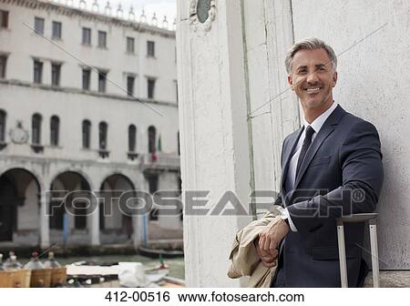 Stock Photograph - Portrait of smiling businessman with suitcase in Venice. Fotosearch
