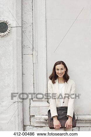 Stock Photograph - Portrait of smiling businesswoman leaning against building wall. Fotosearch