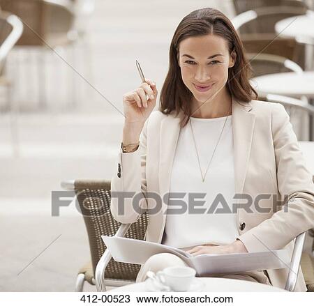 Stock Image - Portrait of smiling businesswoman with paperwork at sidewalk cafe. Fotosearch