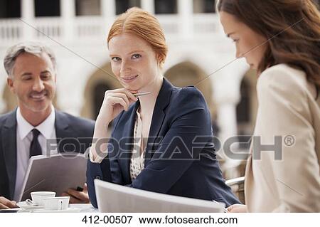 Portrait of smiling businesswomen working with co-workers at sidewalk cafe View Large Photo Image Stock Photo - Portrait of smiling businesswomen working with co-workers at sidewalk cafe. Fotosearch