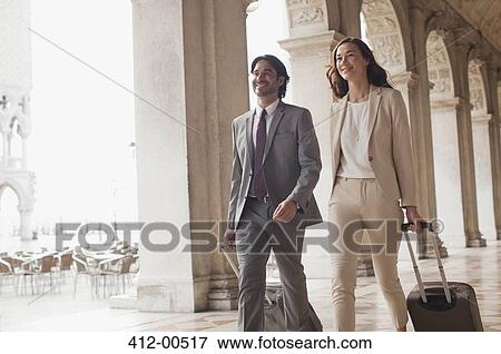 Smiling businessman and businesswoman pulling suitcases along corridor View Large Photo Image Stock Photo - Smiling businessman and businesswoman pulling suitcases along corridor. Fotosearch