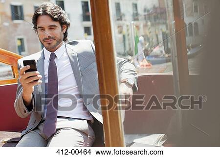 Smiling businessman checking cell phone on boat View Large Photo Image Picture - Smiling businessman checking cell phone on boat. Fotosearch