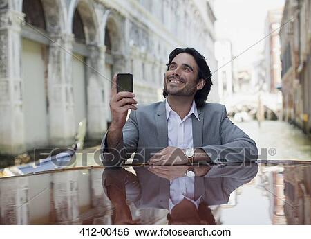 Smiling businessman holding cell phone and leaning on boat in canal in Venice View Large Photo Image Stock Photograph - Smiling businessman holding cell phone and leaning on boat in canal in Venice. Fotosearch