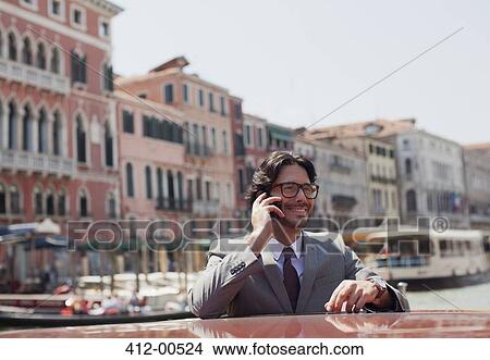 Picture - Smiling businessman talking on cell phone on boat in Venice. Fotosearch
