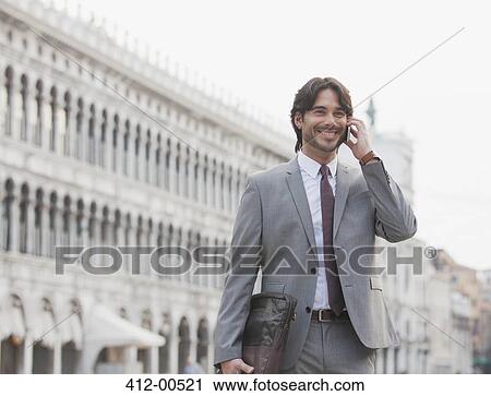 Stock Image - Smiling businessman talking on cell phone in St. Mark's Square in Venice. Fotosearch