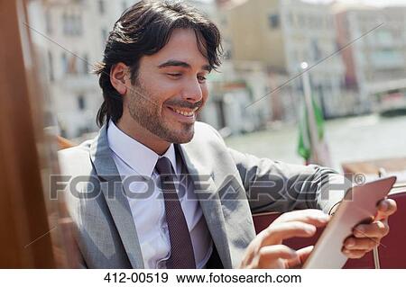 Stock Photo - Smiling businessman using digital tablet on boat in Venice. Fotosearch