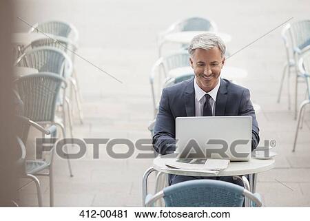 Stock Image - Smiling businessman using laptop at sidewalk cafe. Fotosearch