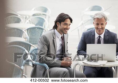 Stock Image - Smiling businessman using laptop at sidewalk cafe. Fotosearch