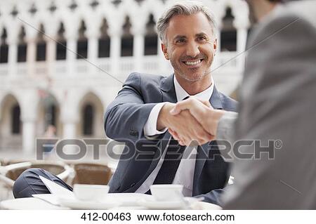 Smiling businessmen shaking hands at sidewalk cafe View Large Photo Image Stock Image - Smiling businessmen shaking hands at sidewalk cafe. Fotosearch