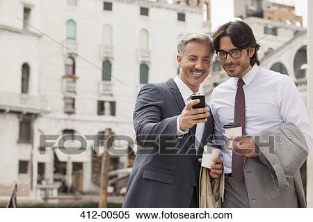 Smiling businessmen with coffee looking down at cell phone in Venice View Large Photo Image Stock Photography - Smiling businessmen with coffee looking down at cell phone in Venice. Fotosearch