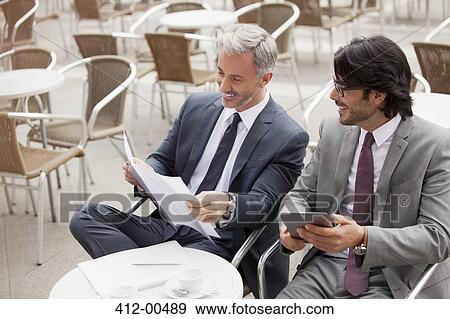 Smiling businessmen with digital tablet and paperwork in cafe View Large Photo Image Stock Photo - Smiling businessmen with digital tablet and paperwork in cafe. Fotosearch