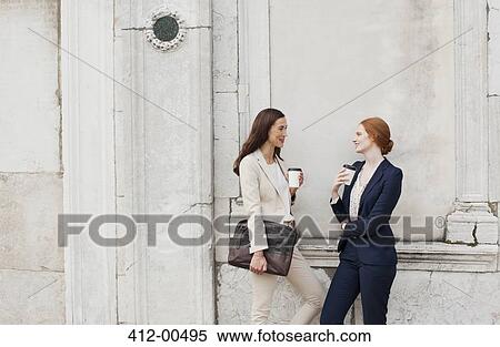 Smiling businesswomen drinking coffee and talking against building wall View Large Photo Image Stock Photography - Smiling businesswomen drinking coffee and talking against building wall. Fotosearch