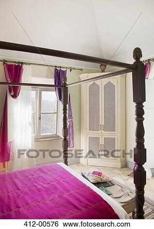 Stock Photograph - Four poster bed with purple bedding in bedroom. Fotosearch