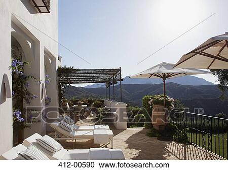 Stock Image - Lounge chairs and umbrellas on balcony of luxury hotel. Fotosearch
