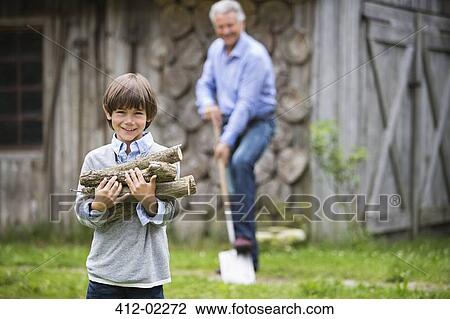 Stock Image - Boy carrying pile of firewood outdoors. Fotosearch