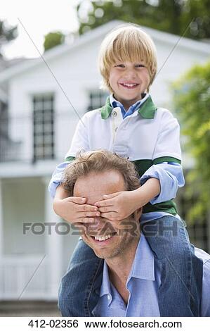 Stock Photograph - Boy covering father's eyes outdoors. Fotosearch
