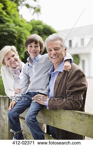 Stock Image - Couple and grandson smiling by wooden fence. Fotosearch