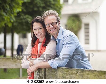 Stock Image - Couple smiling by wooden fence. Fotosearch