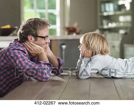 Father and son admiring each other at table View Large Photo Image Stock Photo - Father and son admiring each other at table. Fotosearch