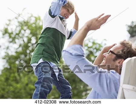 Stock Photo - Father and son high fiving outdoors. Fotosearch