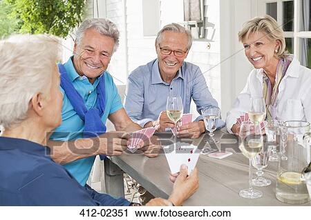 Stock Image - Friends playing card games at table. Fotosearch