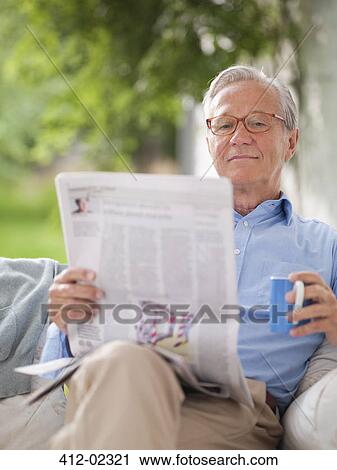 Stock Image - Man reading newspaper in porch swing. Fotosearch