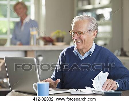 Stock Image - Man using laptop at kitchen table. Fotosearch
