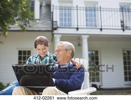 Stock Image - Man using laptop with granddaughter outdoors. Fotosearch