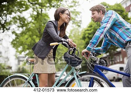 Stock Image - Couple pushing bicycles on city street. Fotosearch