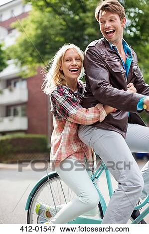 Couple riding bicycle together on city street View Large Photo Image Stock Photo - Couple riding bicycle together on city street. Fotosearch