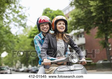 Couple riding scooter together on city street View Large Photo Image Stock Photography - Couple riding scooter together on city street. Fotosearch