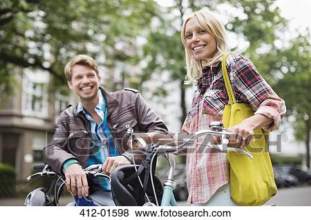 Couple standing on bicycles on city street View Large Photo Image Stock Photo - Couple standing on bicycles on city street. Fotosearch