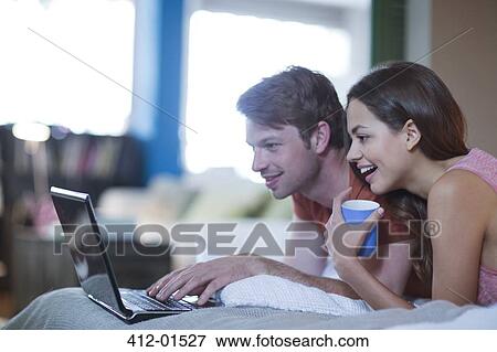 Stock Photo - Couple using laptop together on bed. Fotosearch