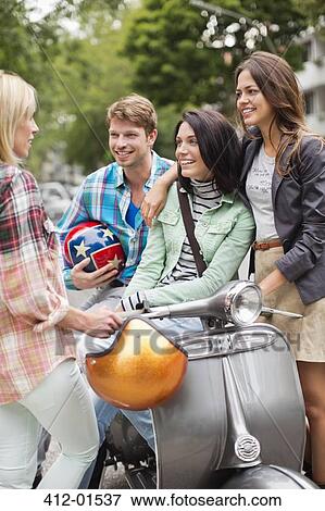Stock Photo - Friends sitting on scooter outdoors. Fotosearch