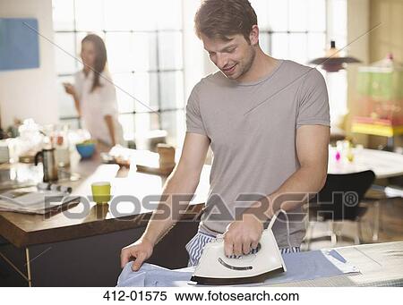 Stock Photography - Man ironing shirt in kitchen. Fotosearch