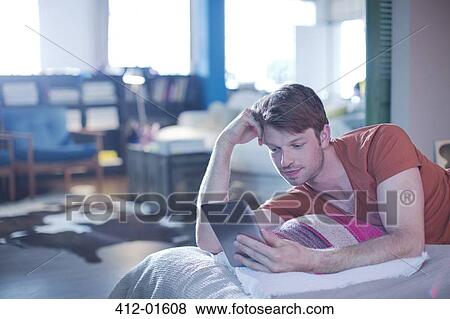 Man using digital tablet on bed View Large Photo Image Stock Photo - Man using digital tablet on bed. Fotosearch