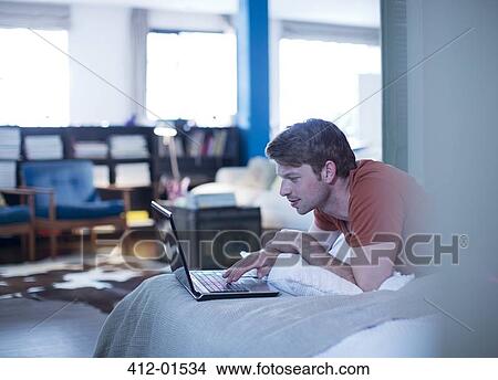 Man using laptop on bed View Large Photo Image Picture - Man using laptop on bed. Fotosearch