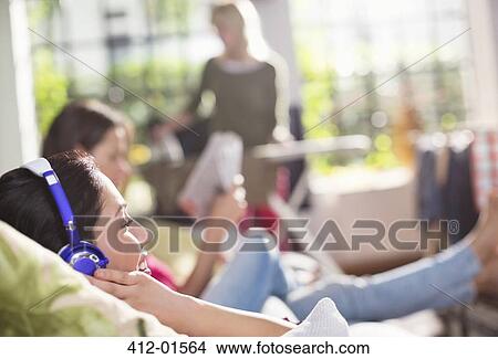 Picture - Woman listening to headphones on sofa. Fotosearch
