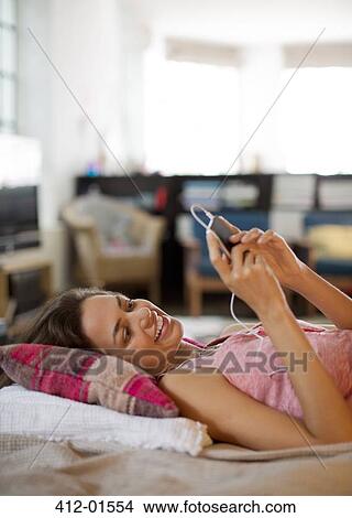 Woman listening to mp3 player on bed View Large Photo Image Picture - Woman listening to mp3 player on bed. Fotosearch