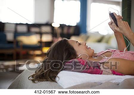 Woman listening to mp3 player on bed View Large Photo Image Stock Photo - Woman listening to mp3 player on bed. Fotosearch