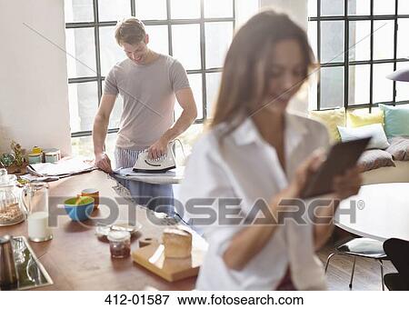 Woman using digital tablet as boyfriend irons in kitchen View Large Photo Image Stock Photo - Woman using digital tablet as boyfriend irons in kitchen. Fotosearch