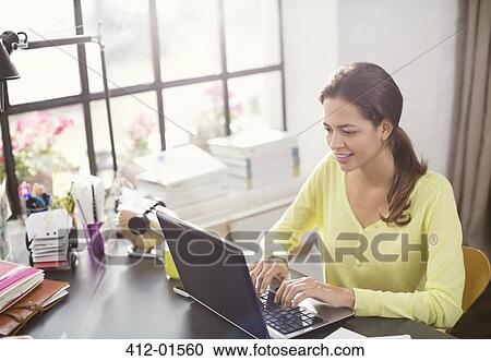 Stock Image - Woman using laptop at desk. Fotosearch