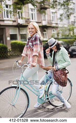 Women riding bicycle together on city street View Large Photo Image Stock Photo - Women riding bicycle together on city street. Fotosearch