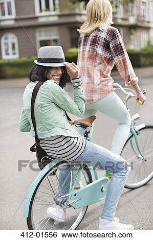 Stock Photograph - Women riding bicycle together on city street. Fotosearch