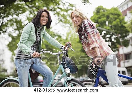 Women sitting on bicycles on city street View Large Photo Image Stock Photography - Women sitting on bicycles on city street. Fotosearch