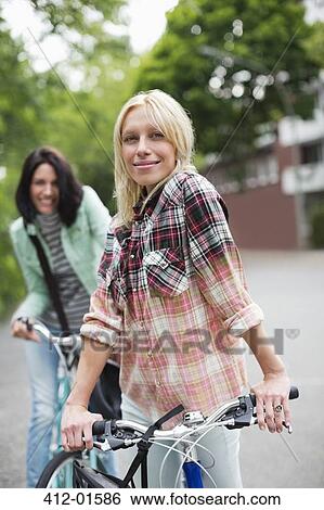 Women standing on bicycles on city street View Large Photo Image Stock Photograph - Women standing on bicycles on city street. Fotosearch
